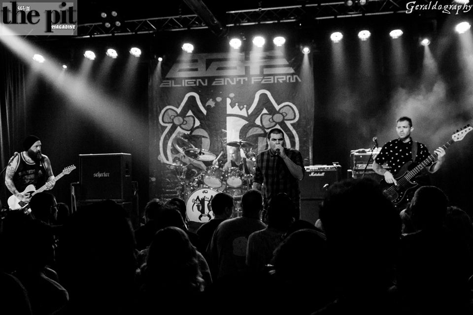Band performing on stage at a concert, audience in foreground, logo "Alien Ant Farm" visible in the background. Black and white photo.