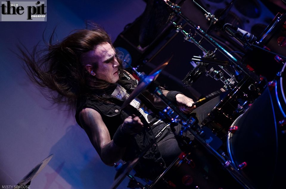 Male drummer with long hair, passionately playing drums on stage for Seven Days Lost, his hair flying around as he moves energetically.