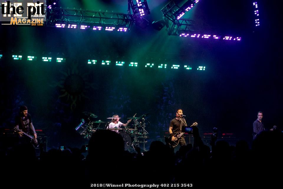 A rock band performs live on stage under vibrant green lighting with the audience in darkness.