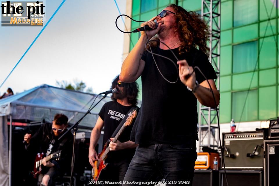 Candlebox performing on stage, with the lead vocalist singing into a microphone and guitarists in the background.