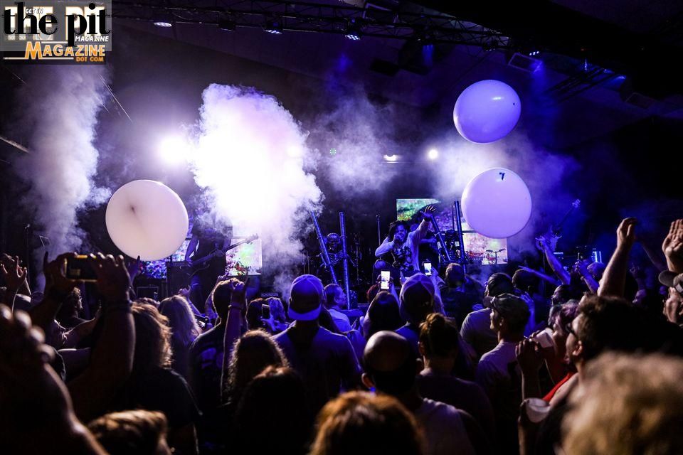 Concert scene with audience looking towards Like a Storm performing under blue lights, accompanied by smoke effects and large white balloons.