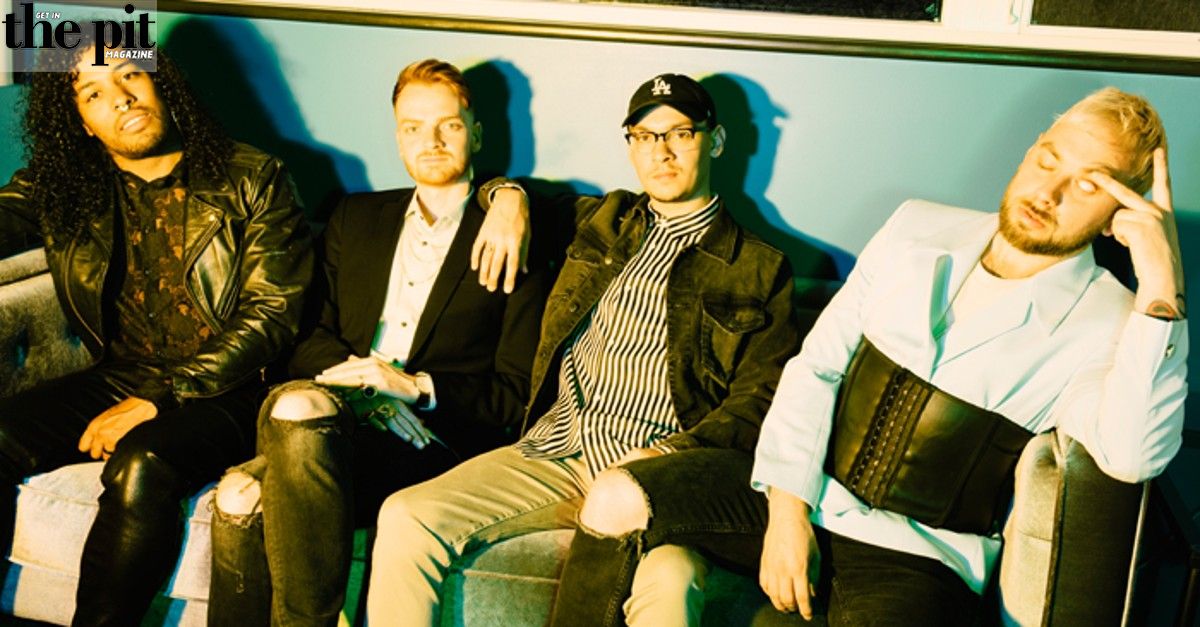 Four men sitting on a couch in a relaxed pose, discussing issues, with one man wearing a leather jacket and another wearing a cap.