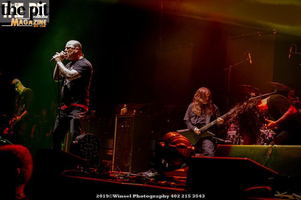 Philip H. Anselmo & The Illegals performing on stage with lead vocalist in focus, other members playing guitar and drums under red stage lighting.