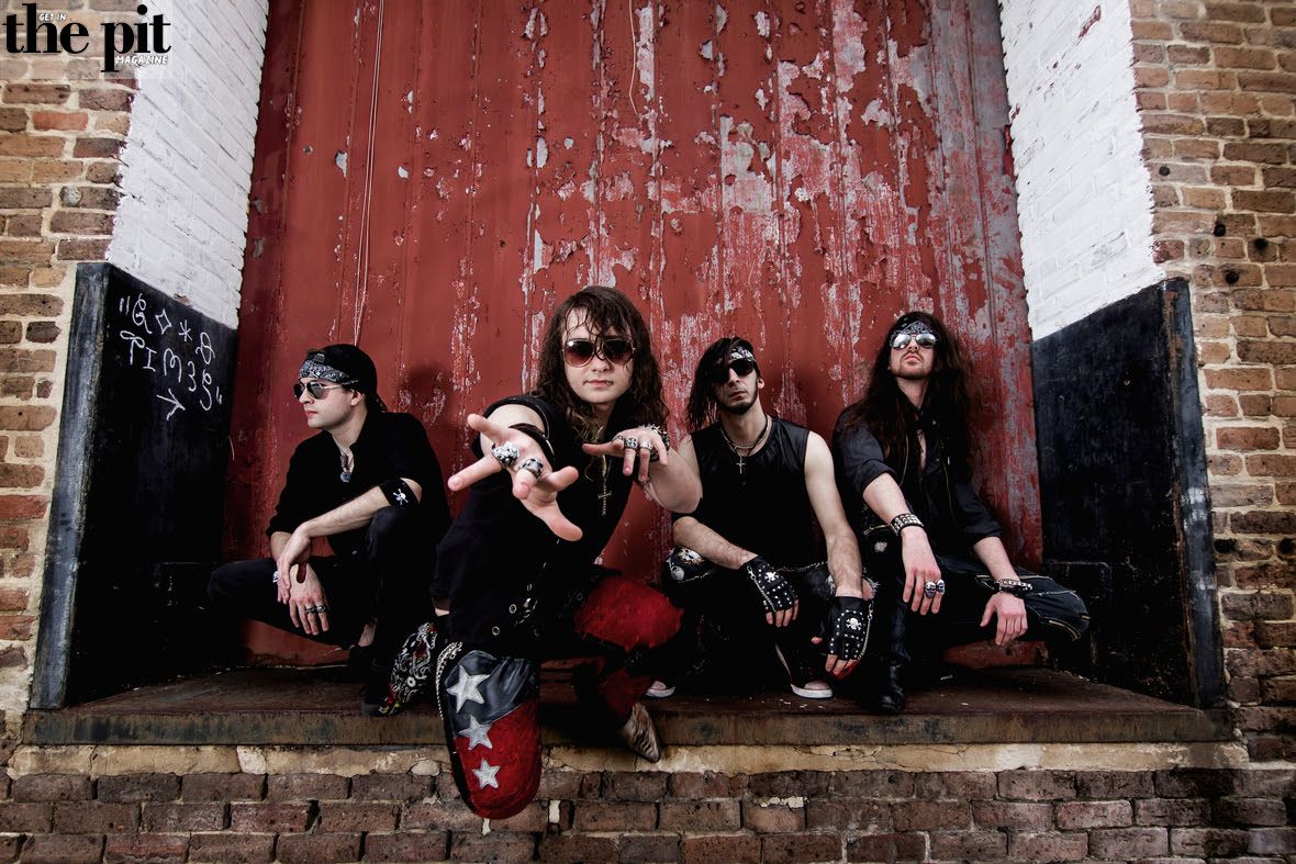 Four members of the rock band Faith & Scars, dressed in edgy outfits, pose confidently against a weathered red and white door.