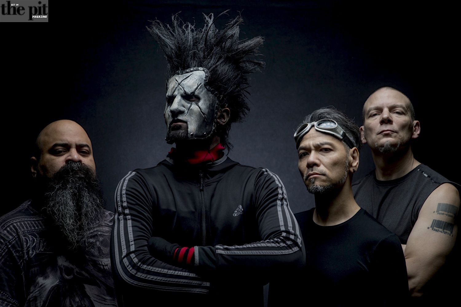 Four men from Static X posing for a photo, one with elaborate black and white face makeup and spiked hair, others with intense expressions, set against a dark background.
