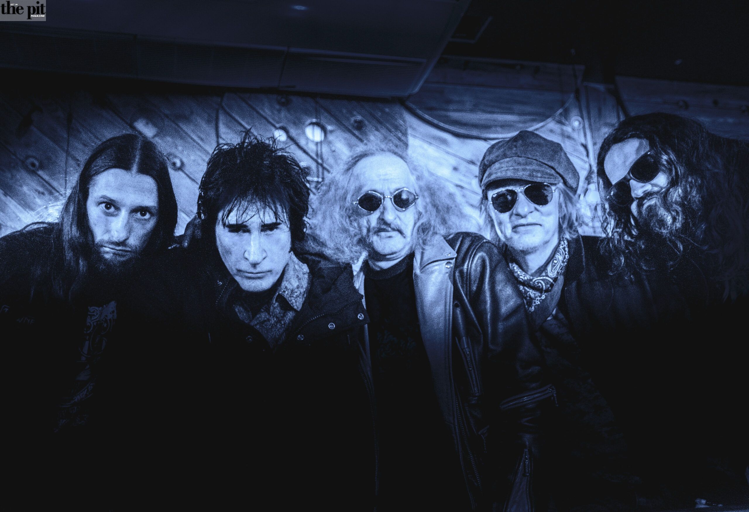 Five members of The Limit, a rock band, posing under blue stage lighting, with serious expressions, wearing dark, eclectic outfits.