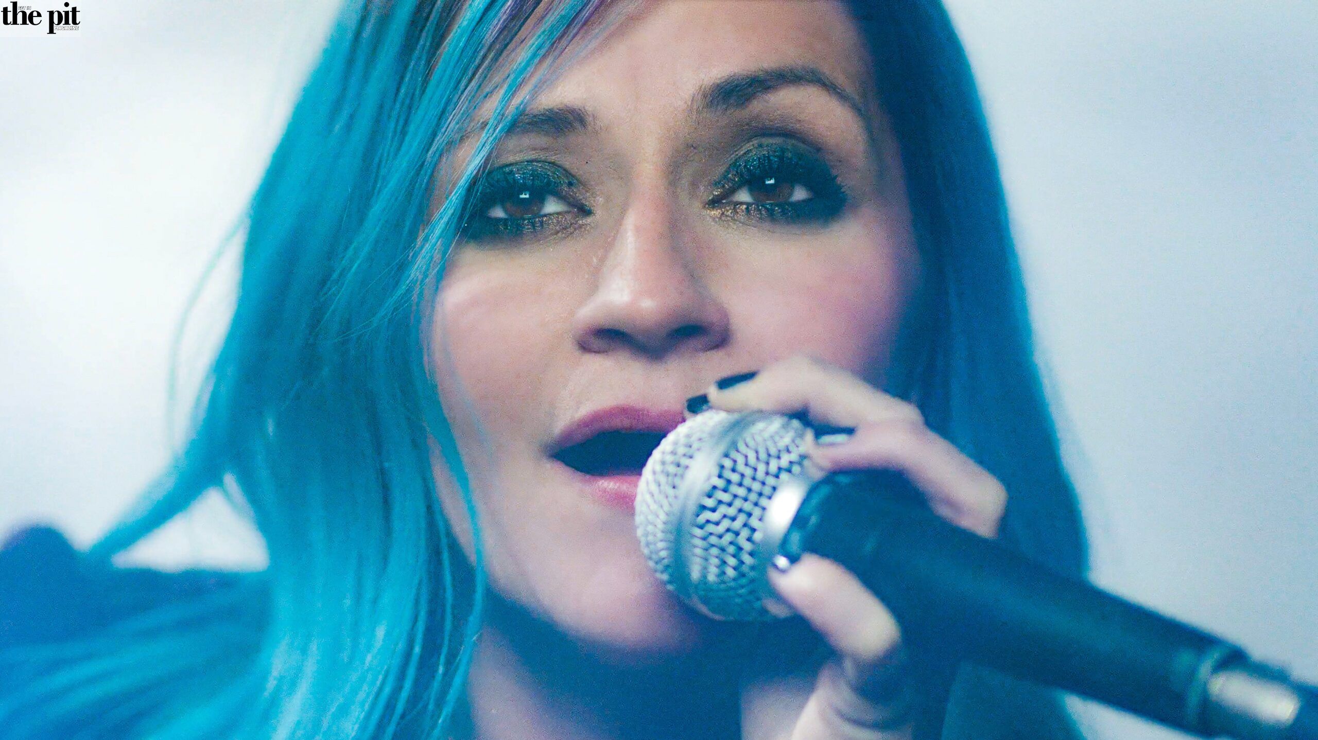 Lacey Sturm, a woman with blue hair singing into a microphone, intense expression, close-up view.