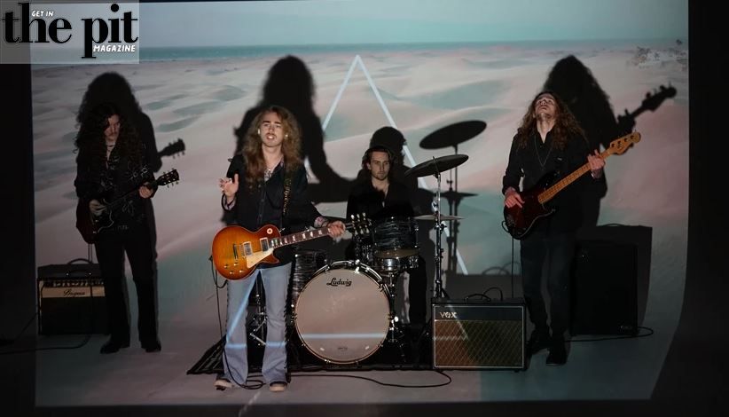 Griffin Tucker & The Real Rock Revolution perform on stage, featuring a guitarist, vocalist, drummer, and bassist, with a soft-toned desert backdrop behind them.
