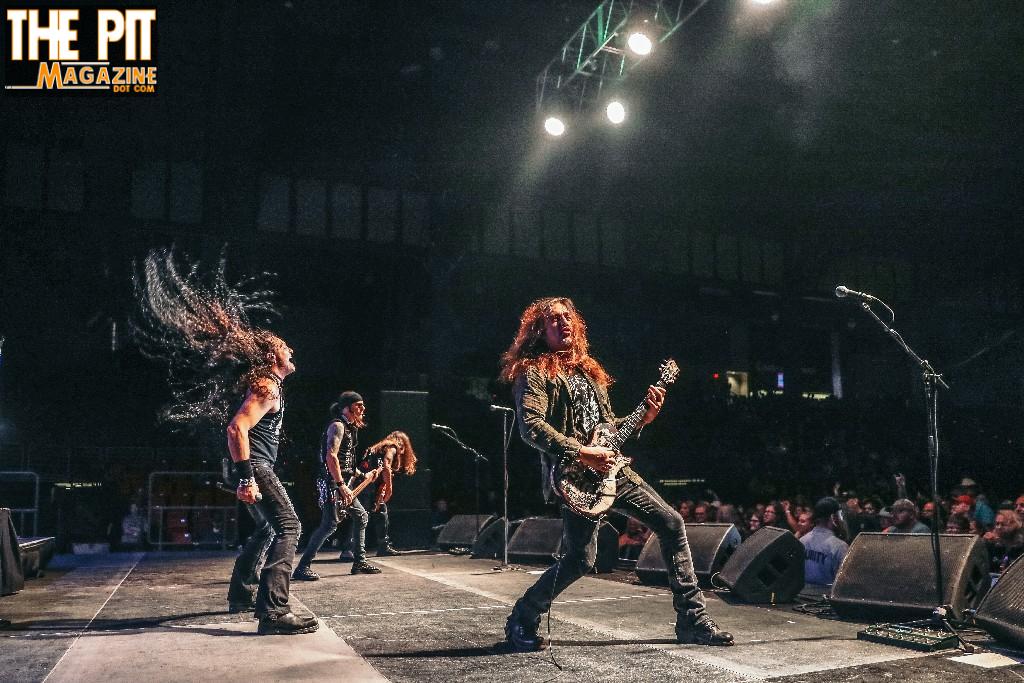 Skid Row band performing on stage, guitarist and bassist with long hair headbanging under bright stage lights, audience in background.