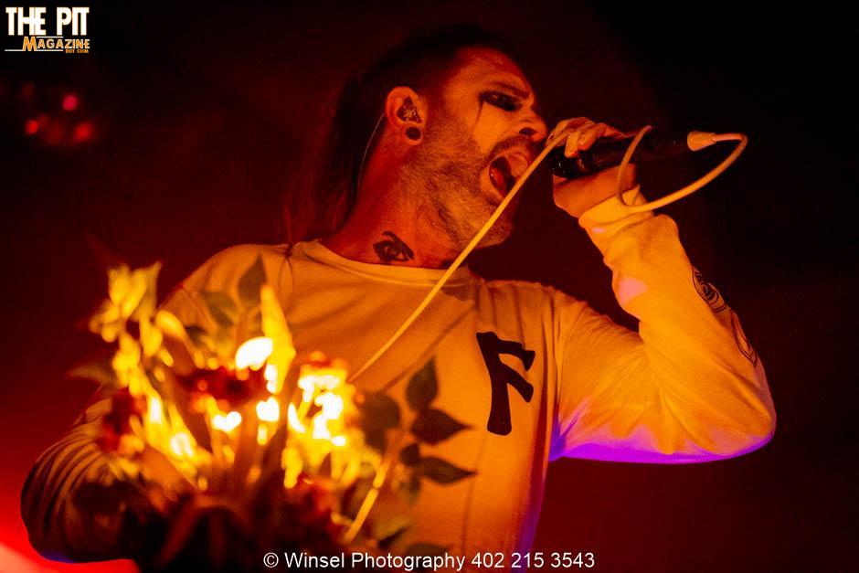 A male singer with tattoos and a microphone performs intensely under red stage lighting at an All Hail The Yeti concert.