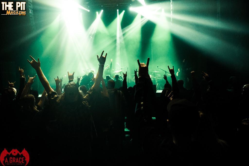 Audience at a Baptize Tour 2021 concert with raised hands, silhouetted against bright stage lights in hues of green and blue.