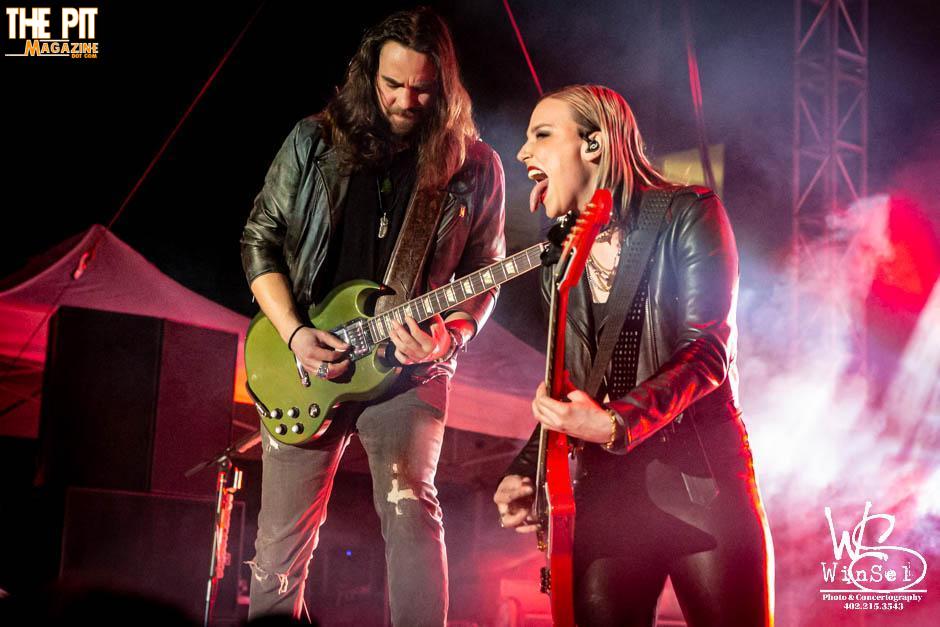 A male guitarist and a female vocalist from Halestorm passionately performing on stage, both dressed in black with vibrant stage lighting.