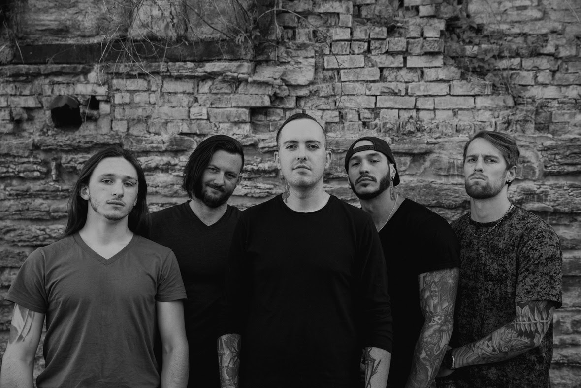 Five men standing in front of a brick wall, looking directly at the camera. They have a serious expression and casual attire. They are members of the band Sleep Signals.