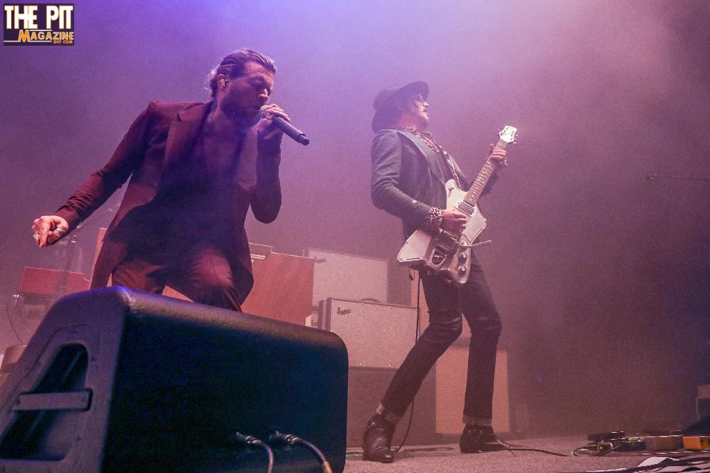Two musicians from Rival Sons performing on stage; one singing into a microphone and the other playing an electric guitar, with atmospheric stage lighting and fog.