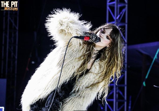 A female singer in a white fur coat passionately singing into a microphone on a concert stage, with dramatic lighting at The Haunt in the background.