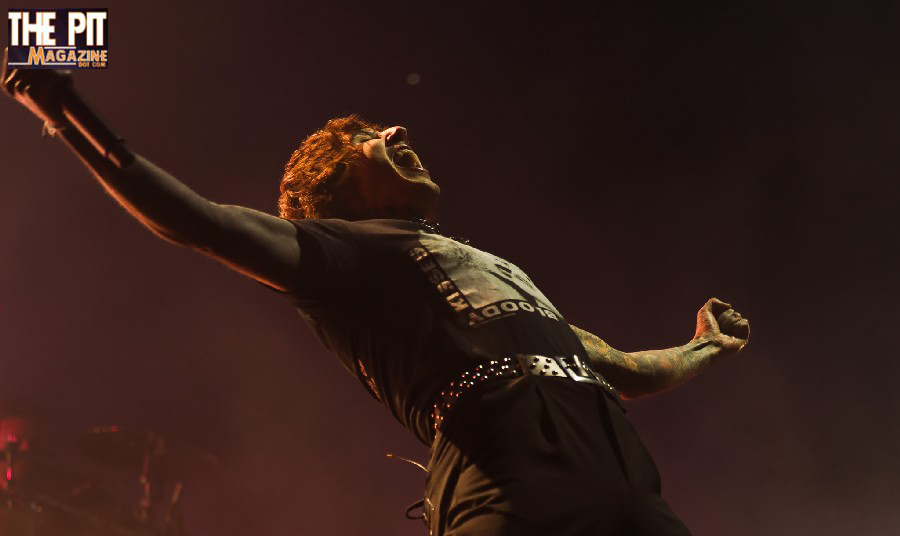 A male rock singer from Bring Me The Horizon passionately performing on stage, bathed in dramatic orange lighting, with his fist raised.
