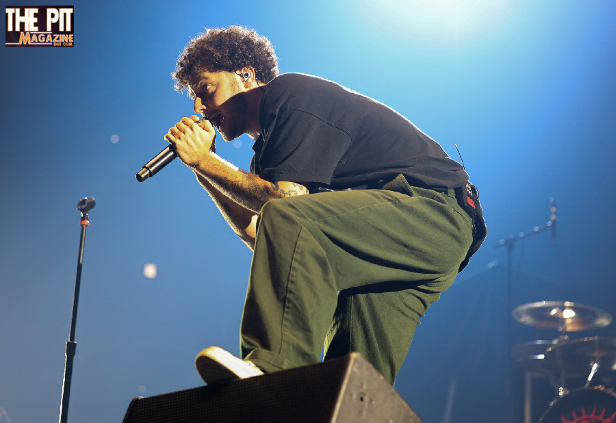 Male singer performing on stage, holding a microphone, with dramatic lighting and a concert stage setup in the background. Grandson accompanies him enthusiastically.