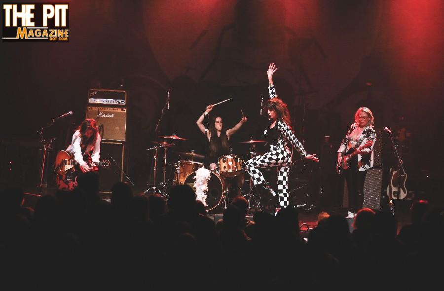 A rock band performs live on stage; the lead singer gestures energetically while band members play guitar and drums, with a logo of "Thunderpussy" overlaying the top left corner.