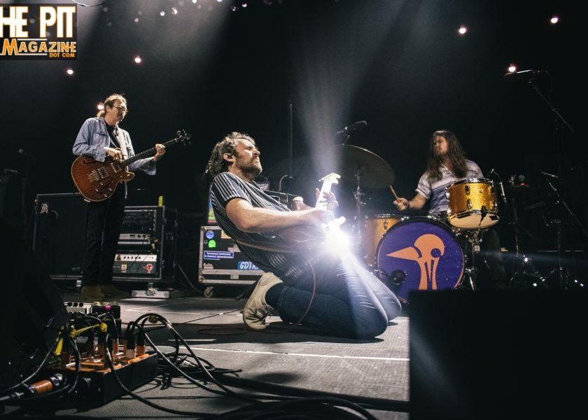 Four men posing for a band photo with 'Get in the Pit Magazine' text.